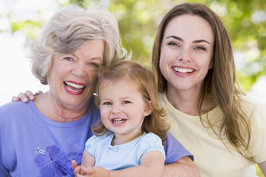 Three generations: a smiling grandmother, an adult daughter, and a young granddaughter posing together outdoors.